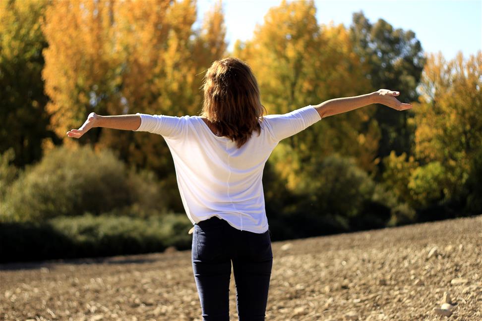 Back of woman with arms out standing in clearing