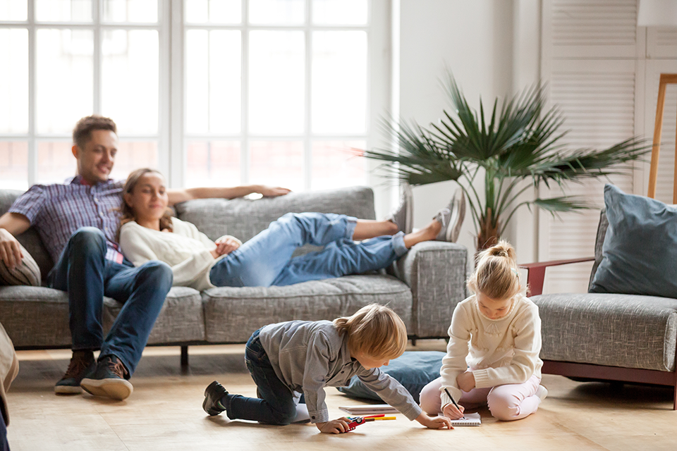 Mom and dad lounging on couch while children color sitting on the floor.