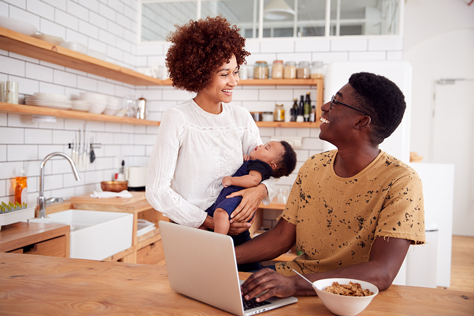 Busy Family In Kitchen At Breakfast With Father Caring For Baby Son