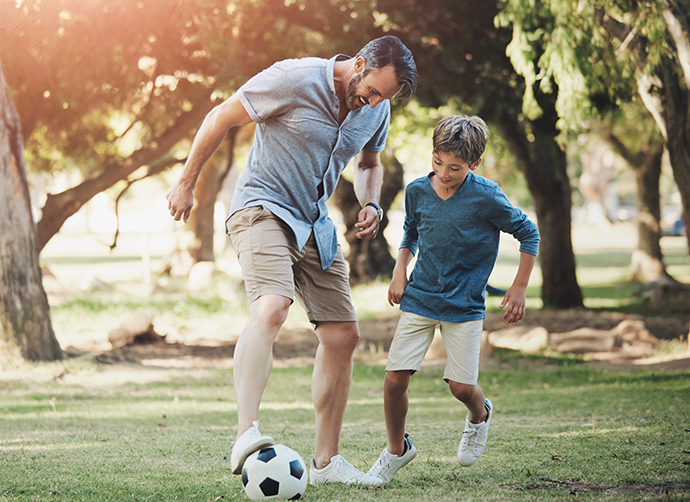 father playing with child in outdoor park practicing soccer