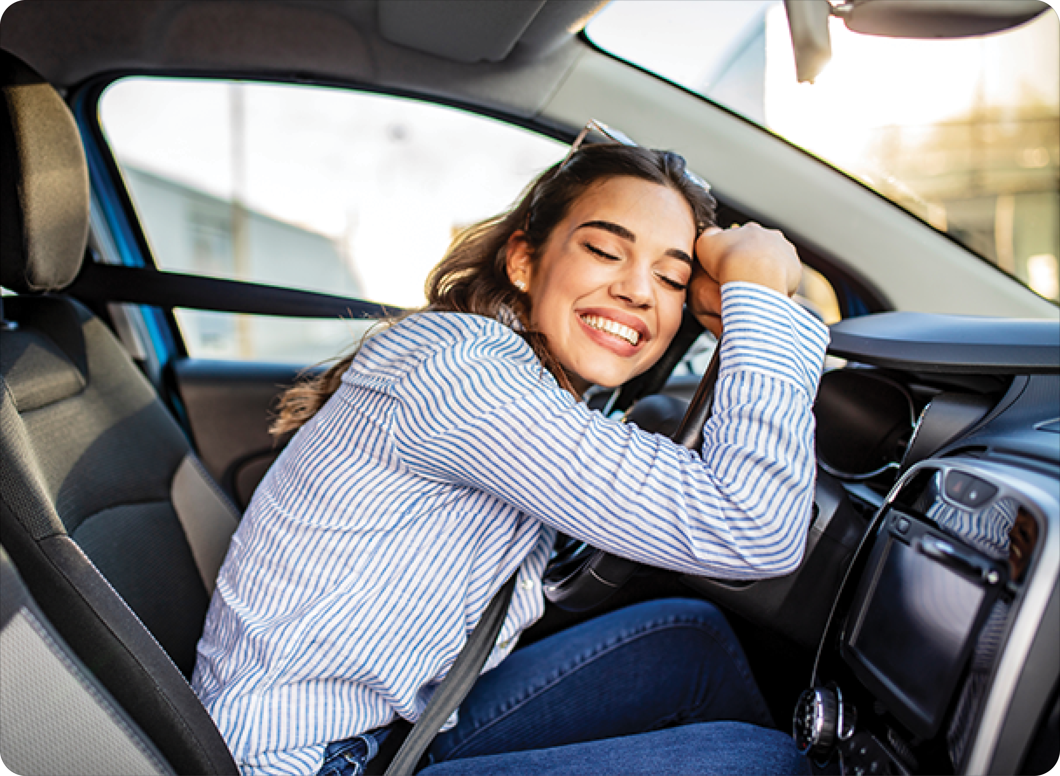 Young and cheerful woman enjoying new car hugging steering wheel sitting inside